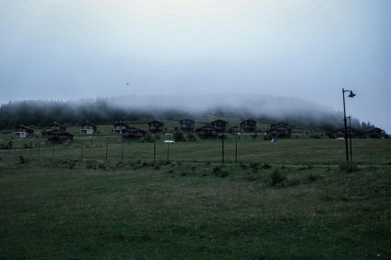 a field with houses in the distance, covered in fog