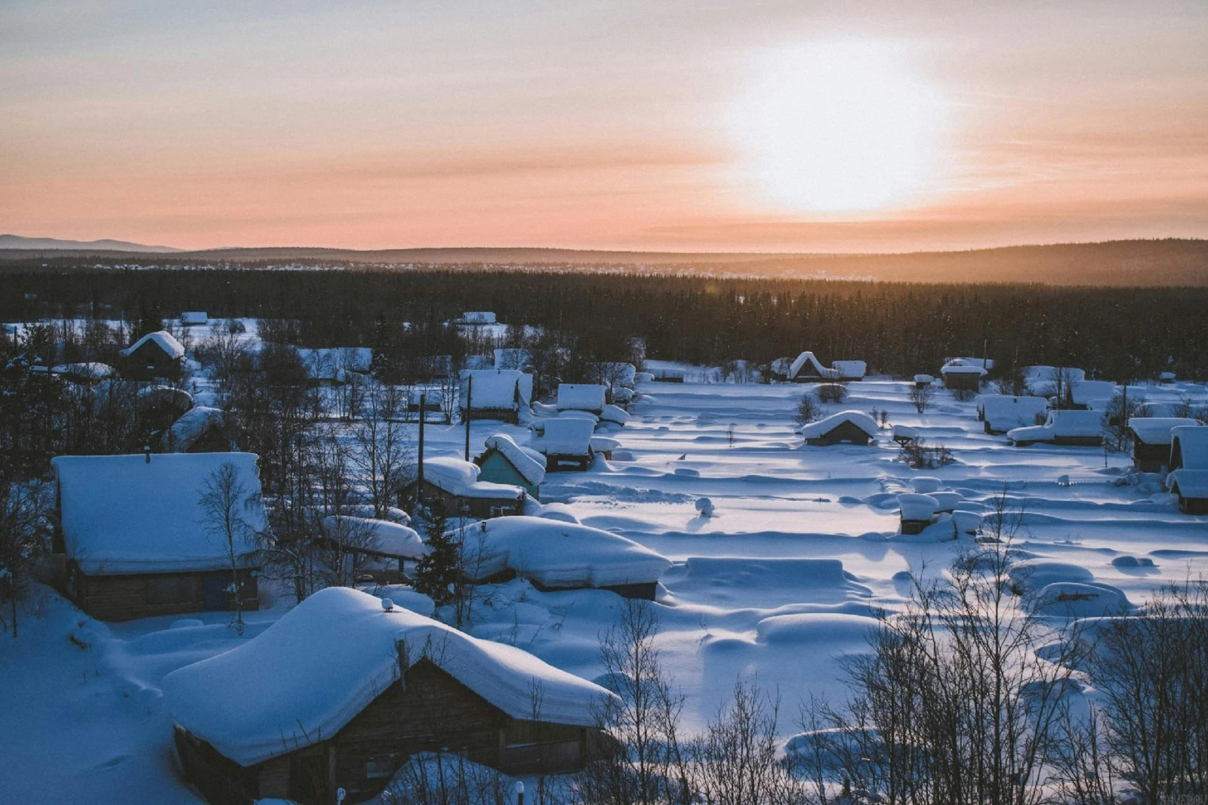 a winter scene of houses in the snow, surrounded by trees