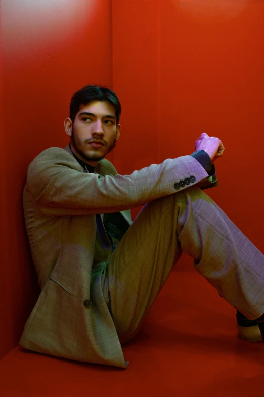 a man sitting against a red wall holding a nintendo wii controller