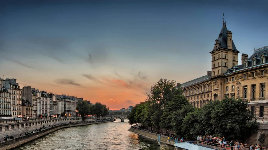 people are standing on the banks as they watch the sun set