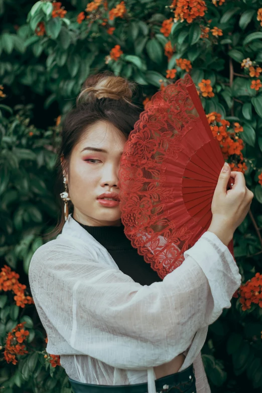 a young woman is standing in front of a bush holding an orange umbrella