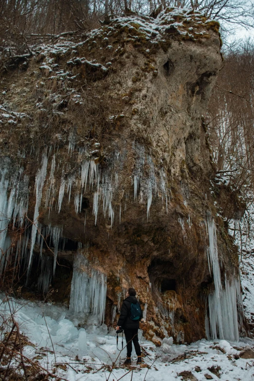 a man standing in front of a very tall cliff covered in ice