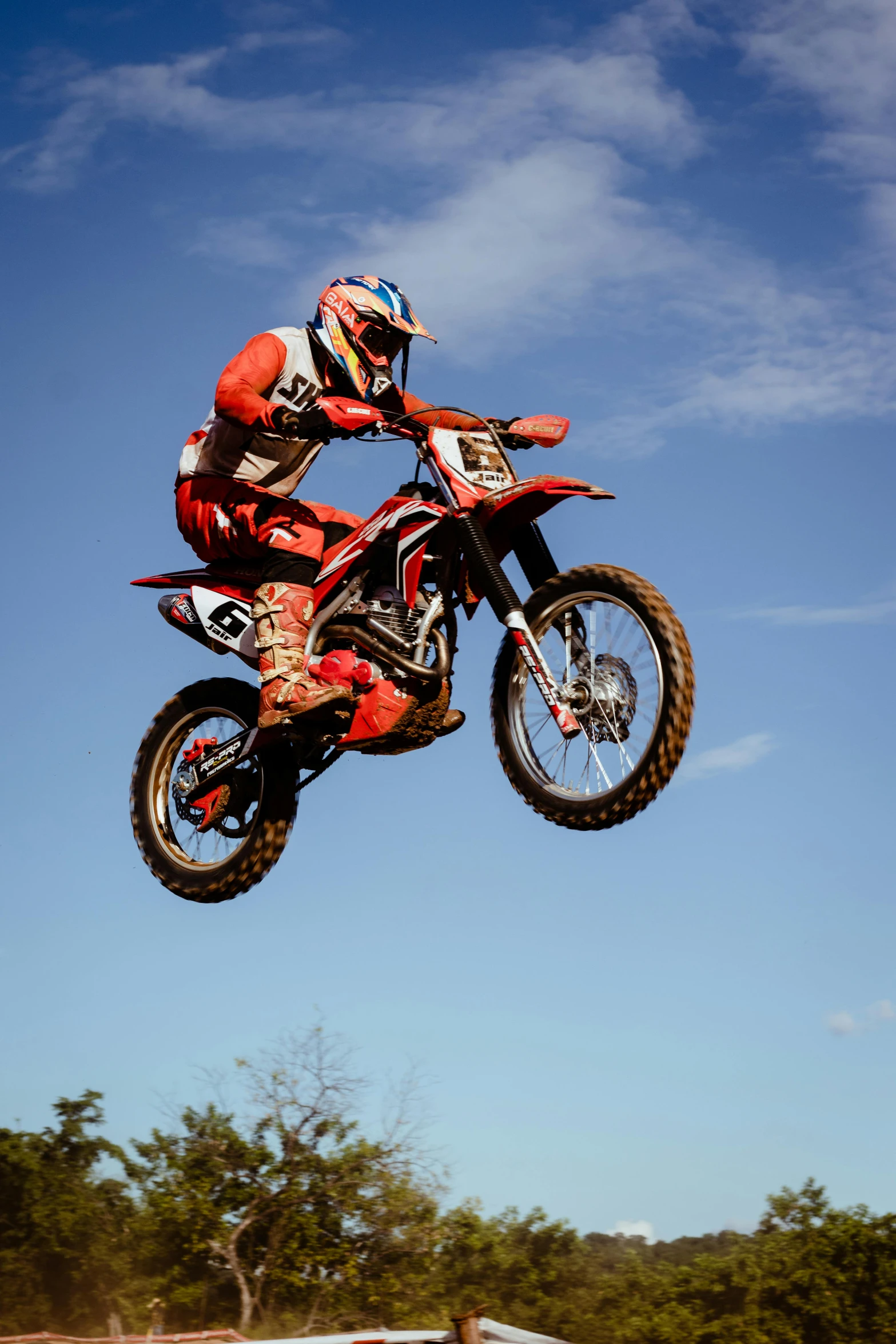 a motorbike rider high up in the air, with trees and grass behind him