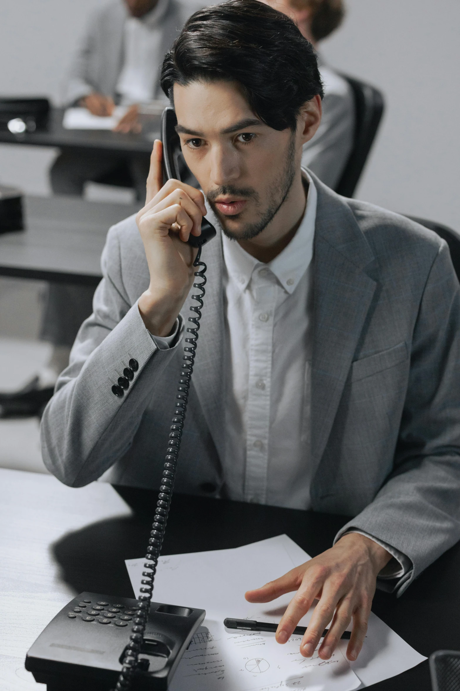 a man sitting at a desk on a telephone with people in the background