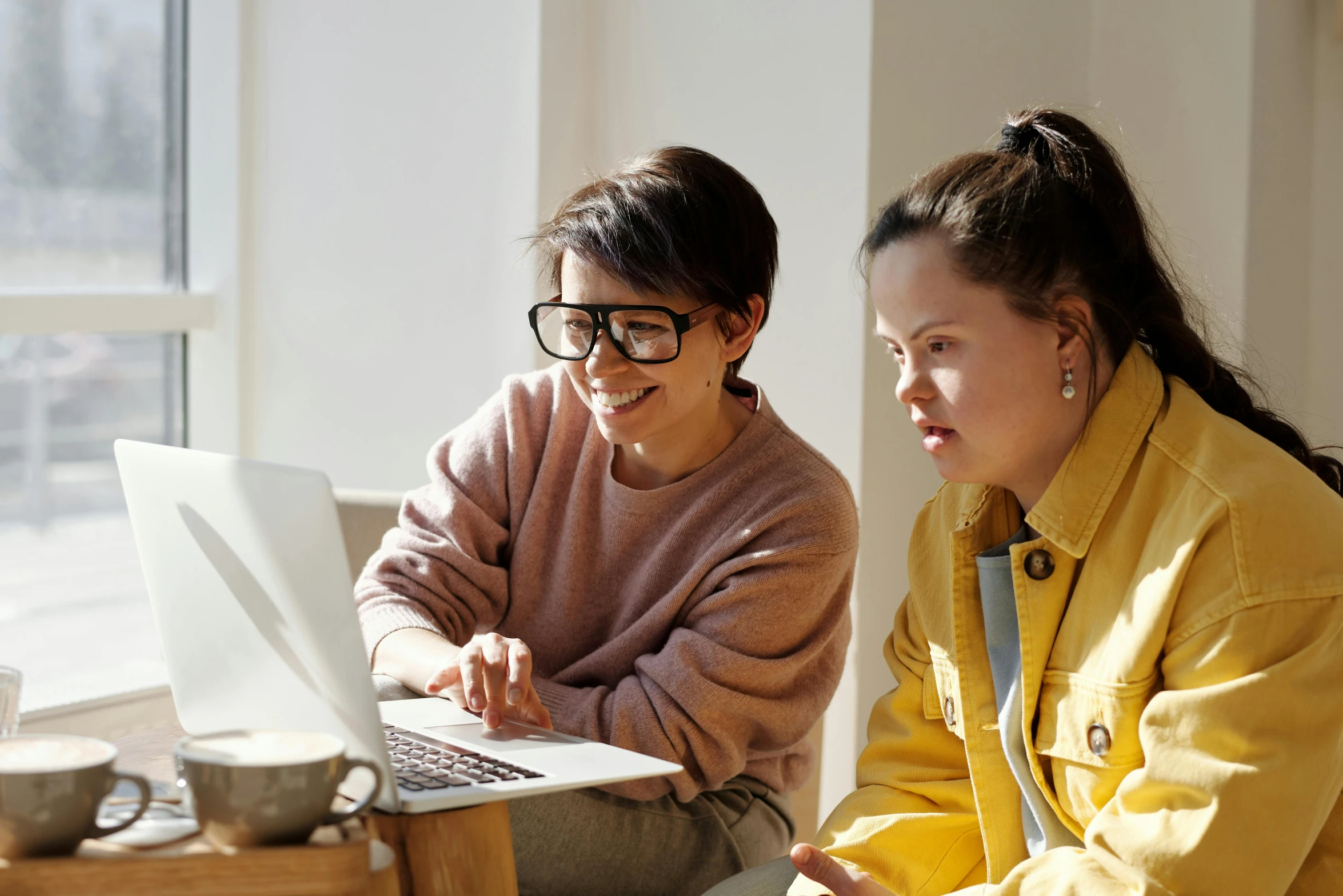 a woman looking at a laptop computer with another smiling