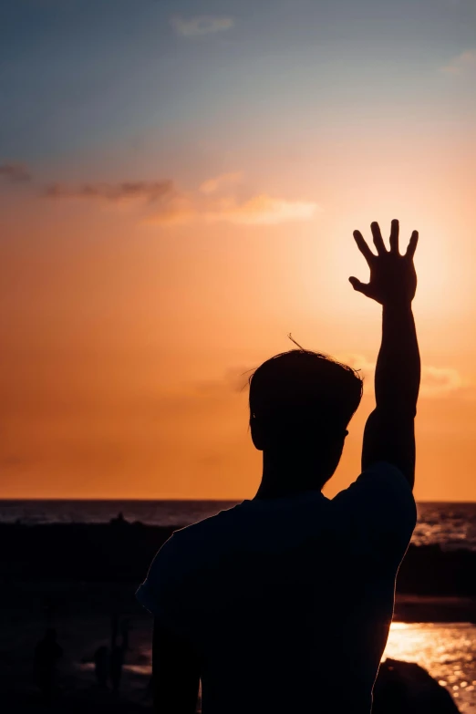 a man raises his hands up into the sky at sunset