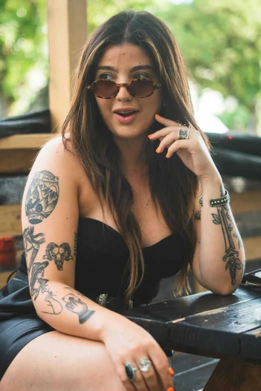 a woman sitting at a table with tattoos on her arm