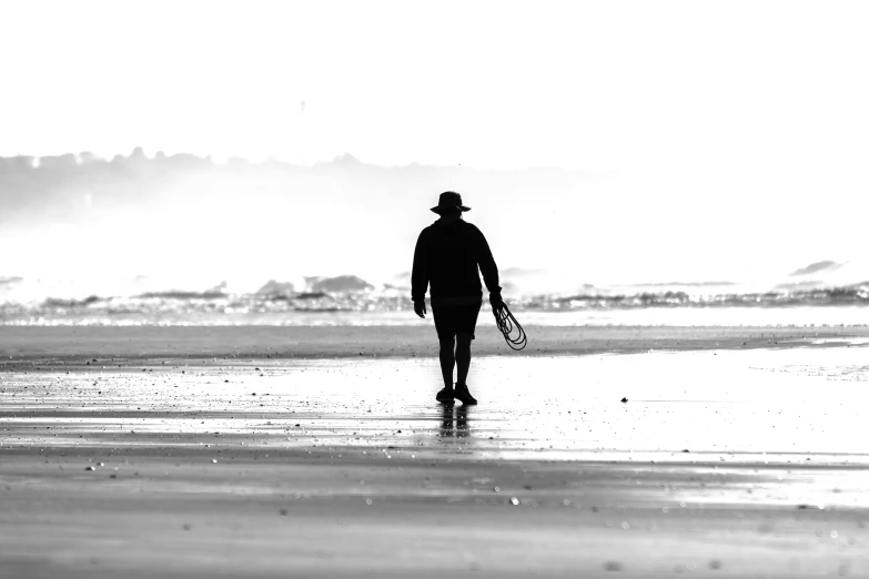 man walking down a beach holding his tennis racquet