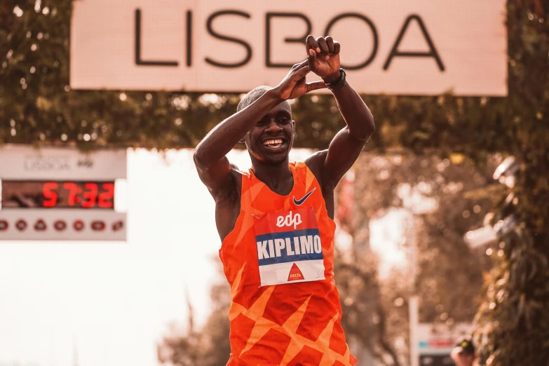 a male athlete dressed in an orange outfit and raising his arm