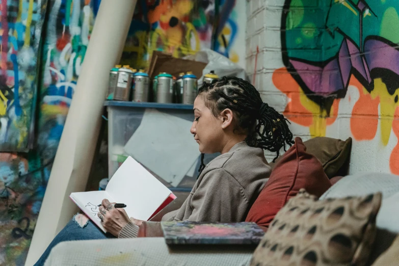 a woman sits with her notebook in front of a graffiti wall