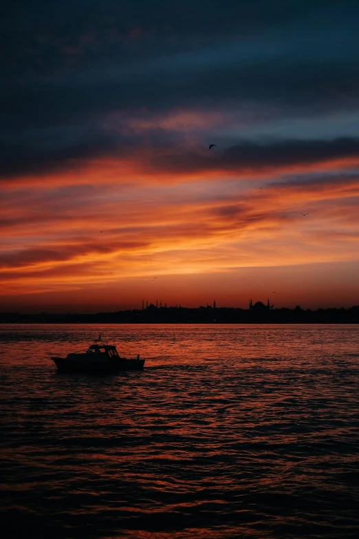 a boat in the ocean at sunset with clouds