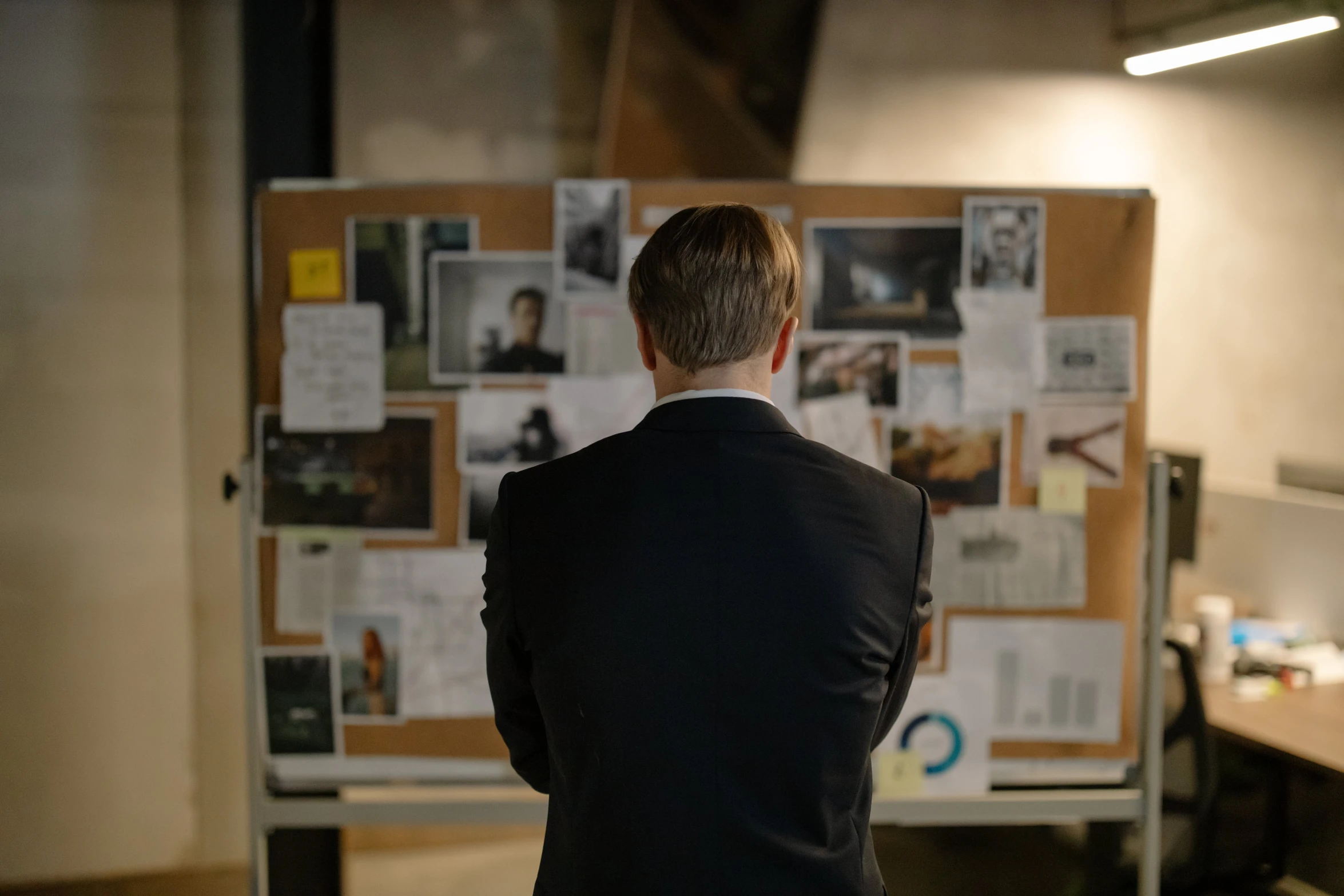 a man in black suit standing by a wall full of papers