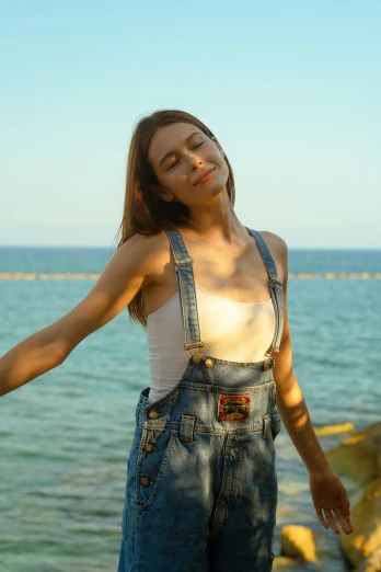 a woman standing by the ocean wearing blue jeans