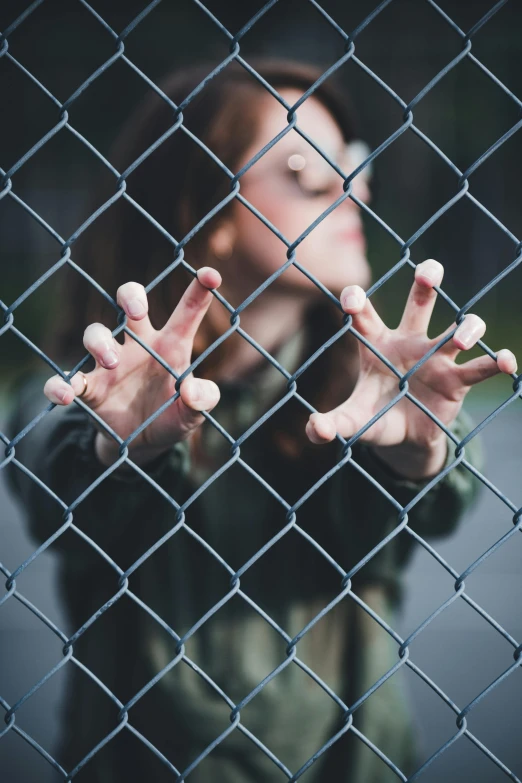 a woman behind a chain link fence with her hands up