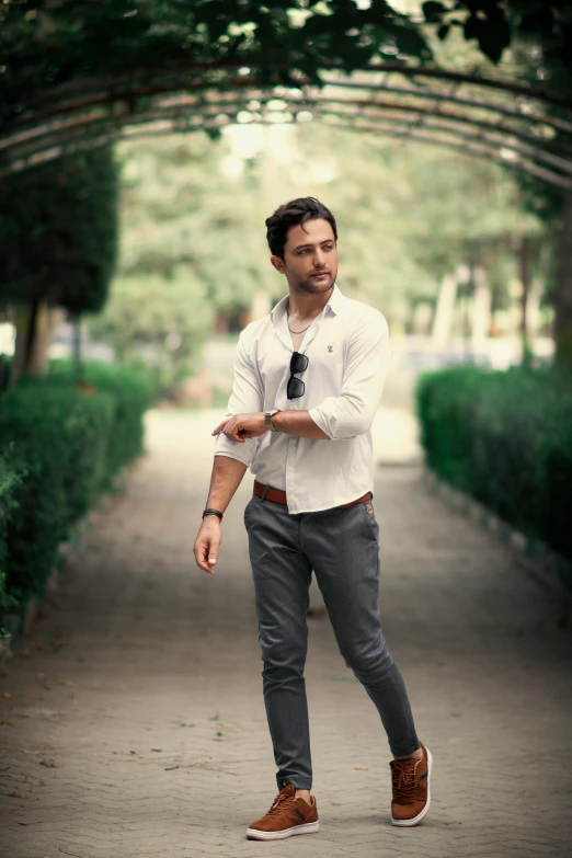 man in white shirt and tie standing under a row of trees