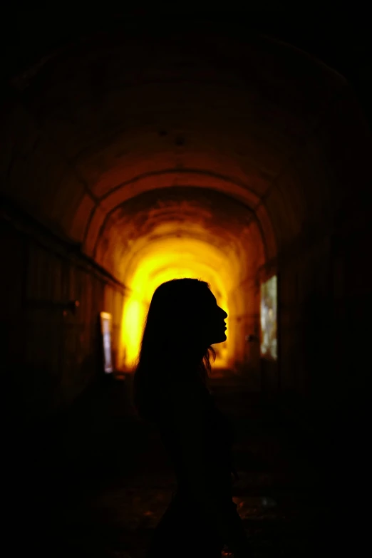 a woman standing inside a dark tunnel with the light going through