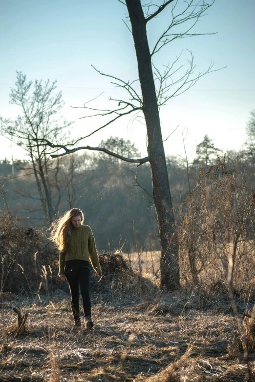 a woman walking in a grassy field next to a forest