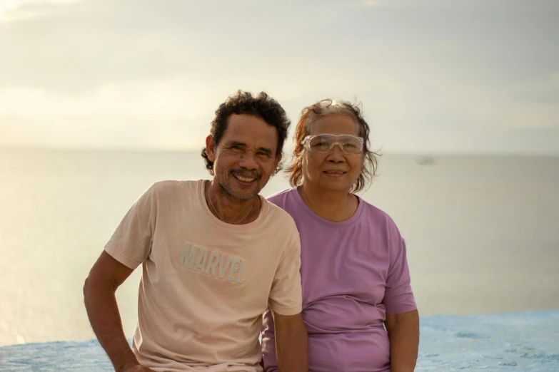 an old man and an old lady posing by the ocean