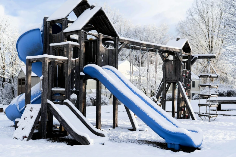 an open play ground covered in snow next to a playground set