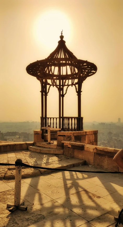 a gazebo with the sun rising over a city in the distance