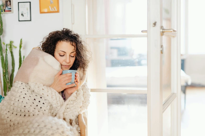 a woman wrapped in a white blanket drinking coffee