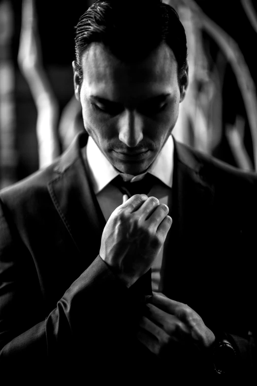 black and white pograph of a man wearing a suit adjusting his tie