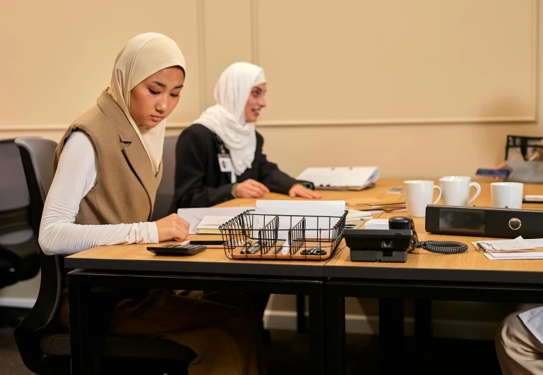 two women are sitting at a table reading and talking