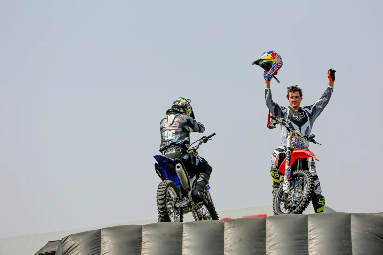 two motorcyclist, one holding up his helmet and the other holding a star