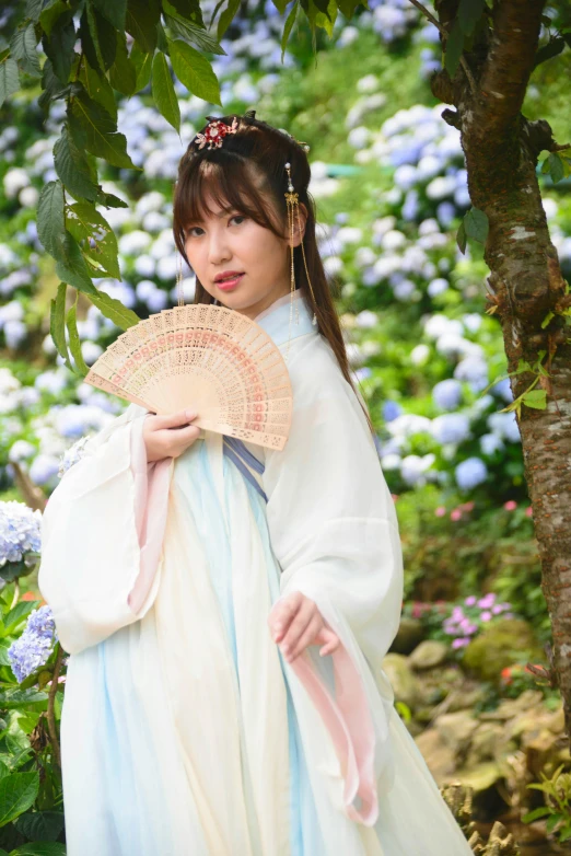 woman in dress and hat holding fan next to tree