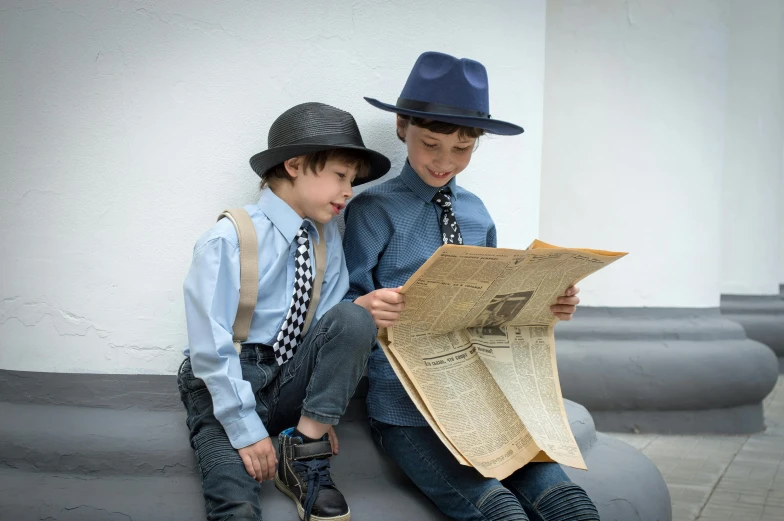 two children sitting on a bench, one wearing a hat and the other reading the paper