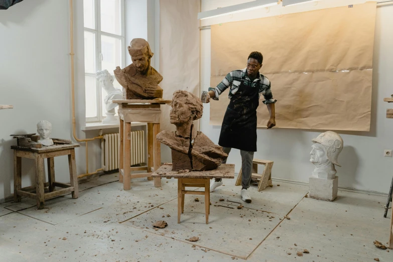 man standing in front of wooden sculptures on pedestals