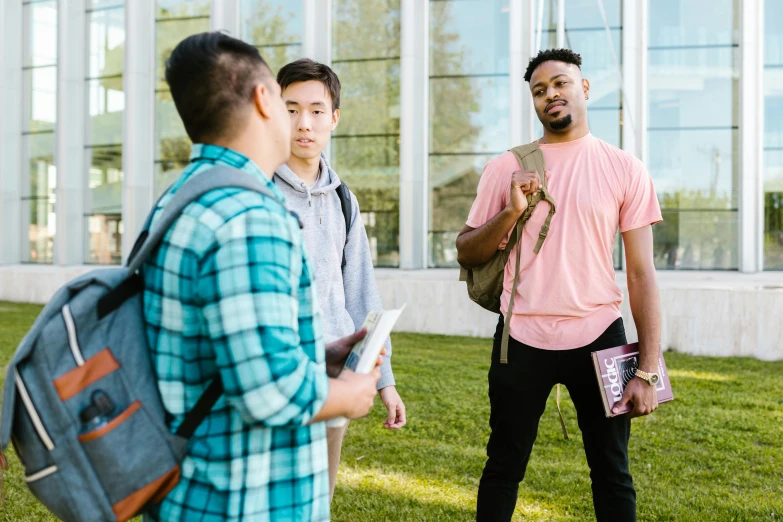 three guys are standing in the grass with backpacks and papers