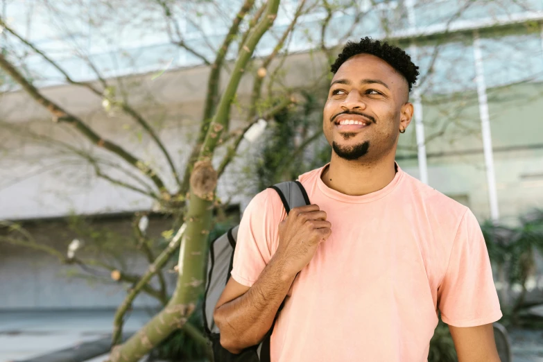 man in pink shirt smiling outside with backpack