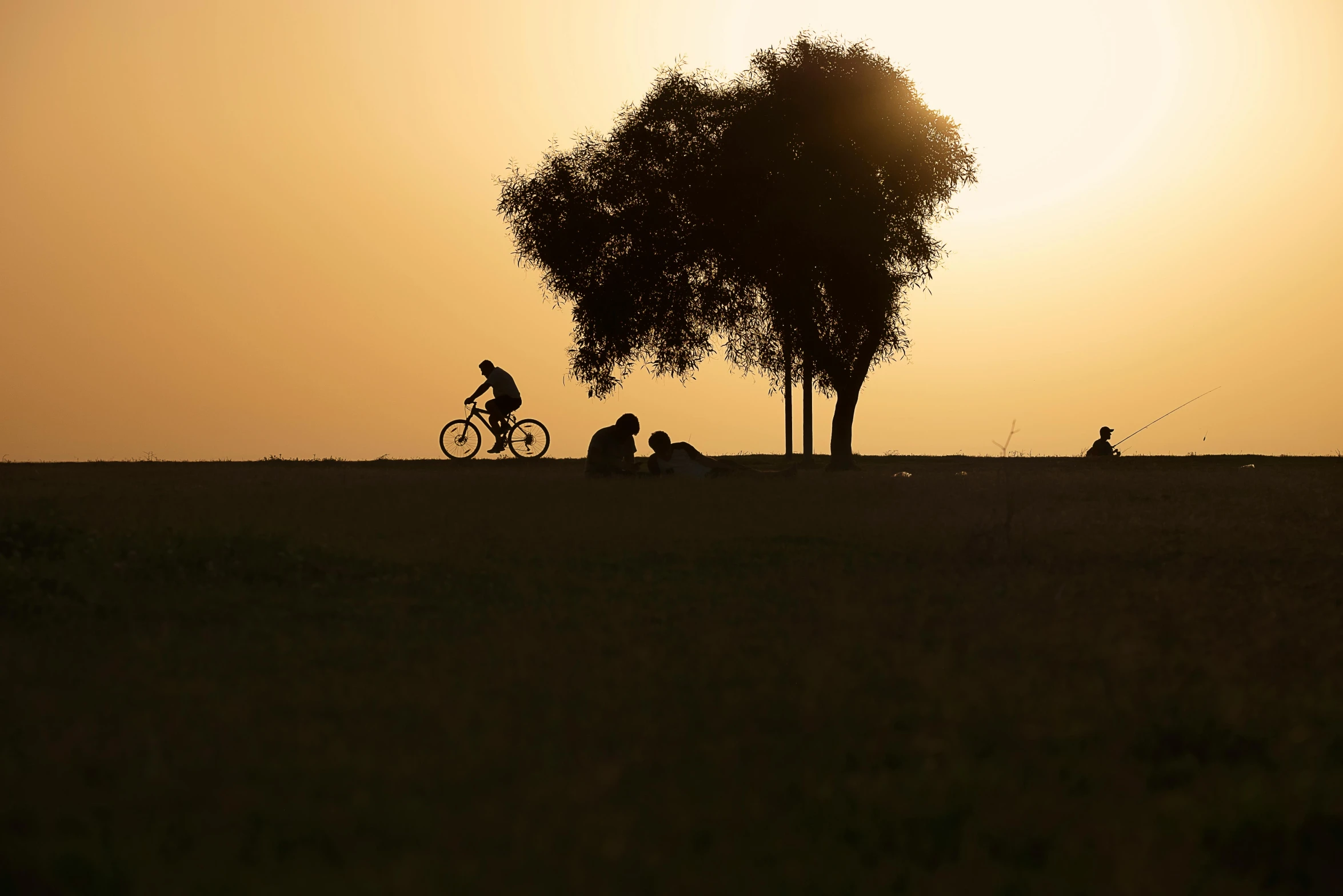 the sun setting in the background while some people sit and watch