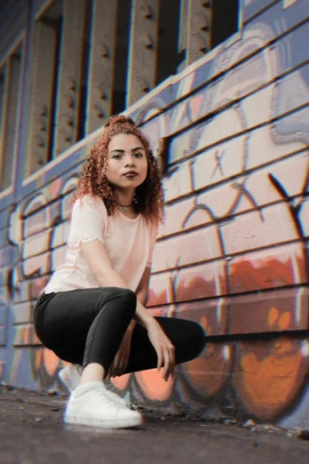 a young lady squatting down by a wall with graffiti on it
