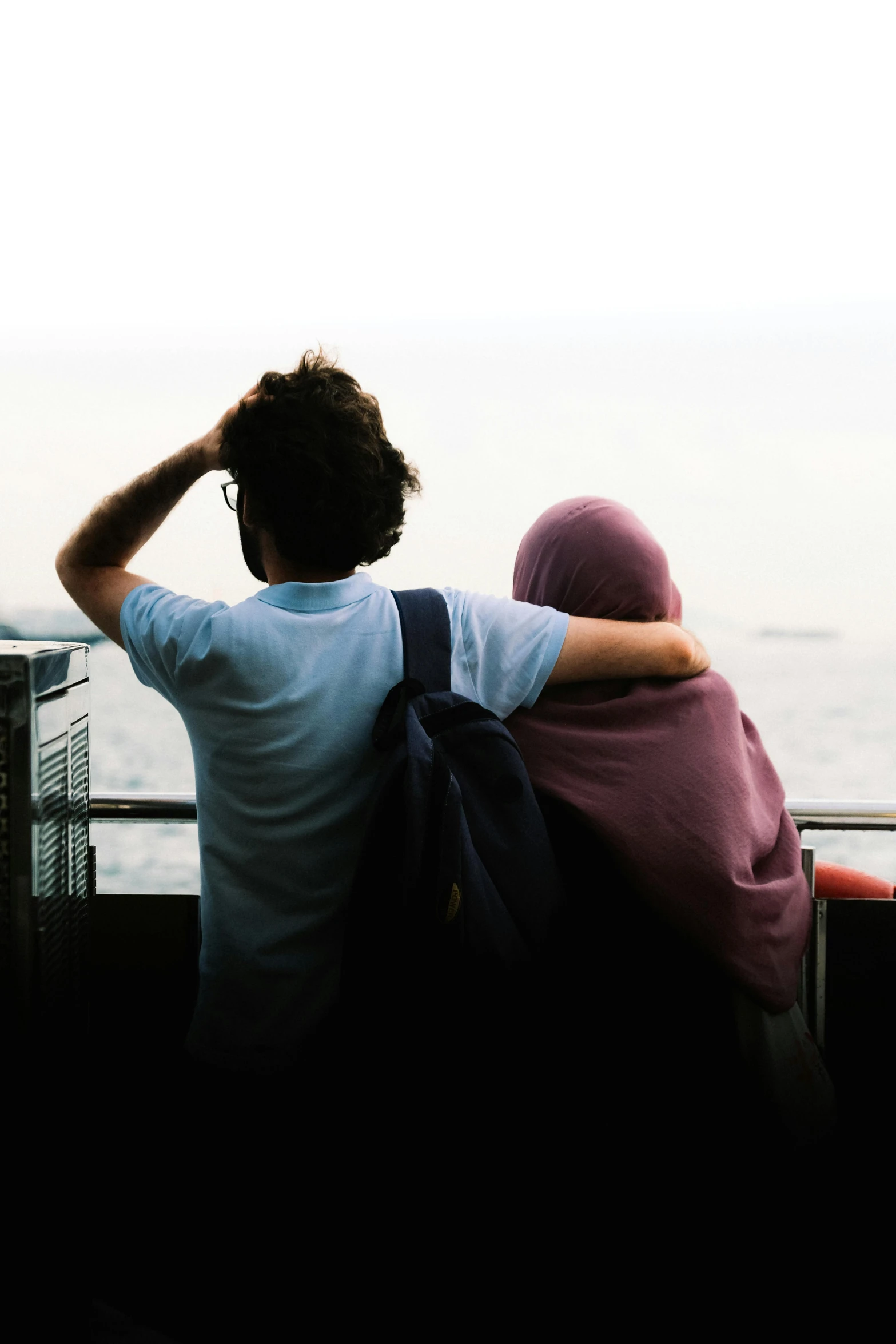 a man and woman sitting on a bench looking at the ocean