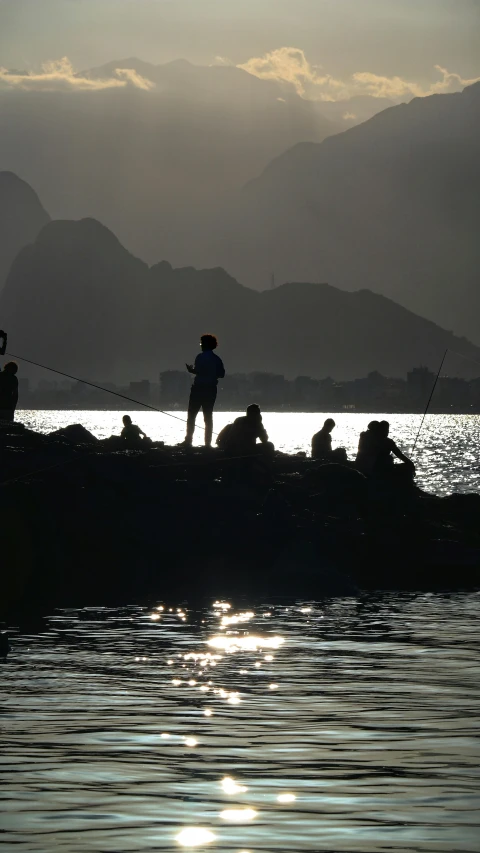 some people sitting on a rocky shore fishing