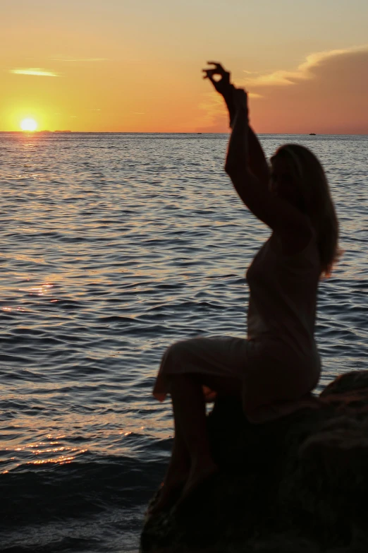 woman on a rock reaching up towards the sky