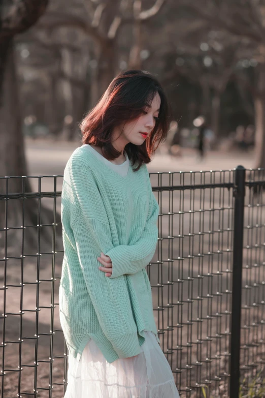 a girl in a light blue sweater leaning on a fence