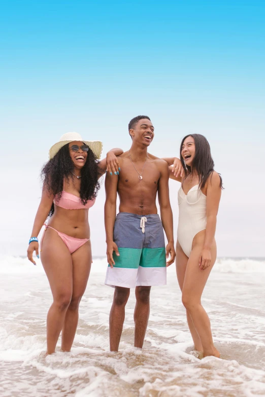 three people in bathing suits and straw hats are standing on the shore of a body of water