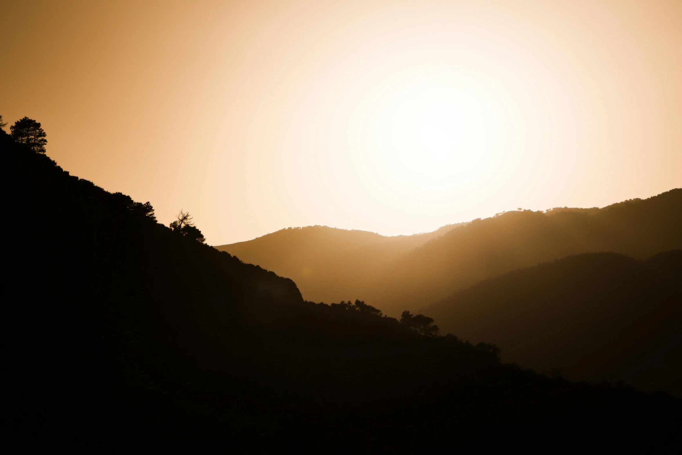 the silhouette of a mountainside with a yellow sun in the sky