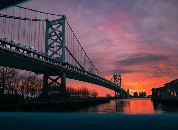 a suspension bridge at sunset in an orange and purple sky