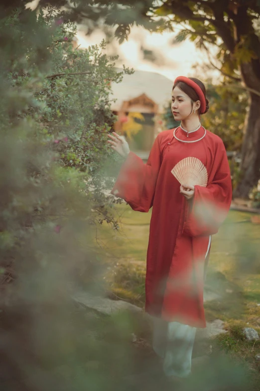 a young asian man in red dress and red hat holding an oriental fan