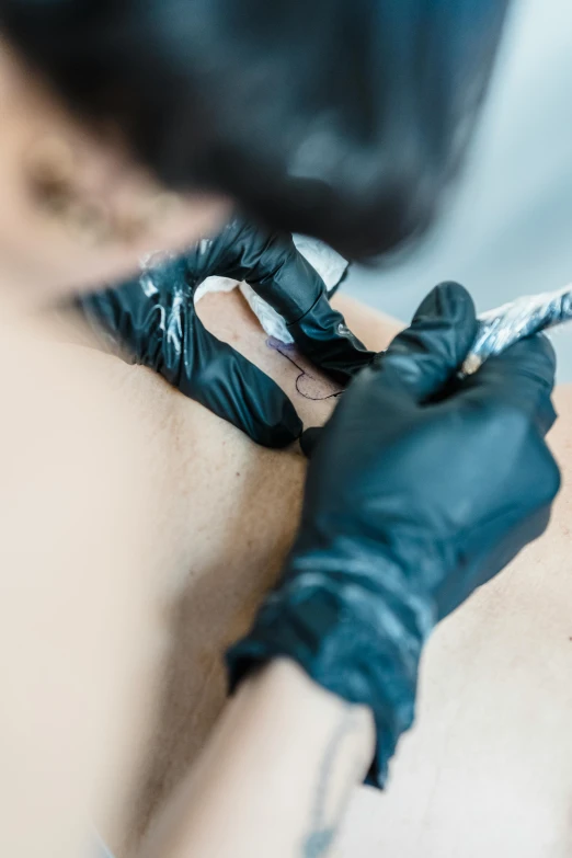 a woman with black gloves is getting her tattoo done
