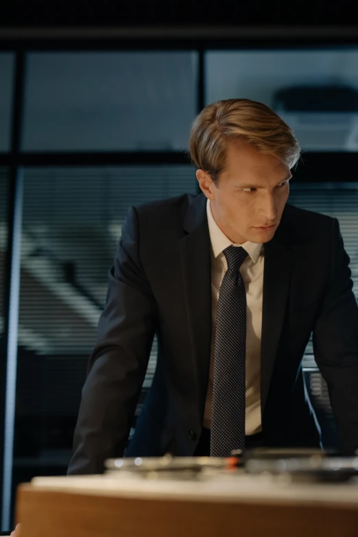 a man in suit and tie sitting at desk with a laptop