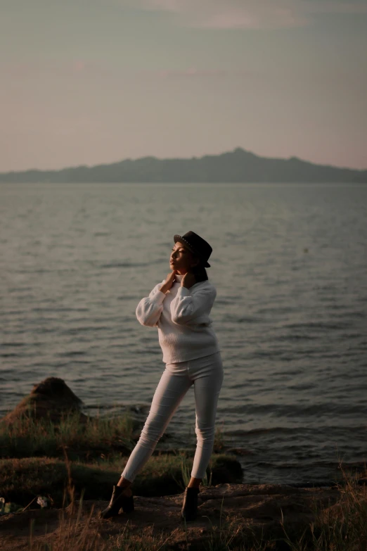 the woman is posing on the shore, with her hands on her hips