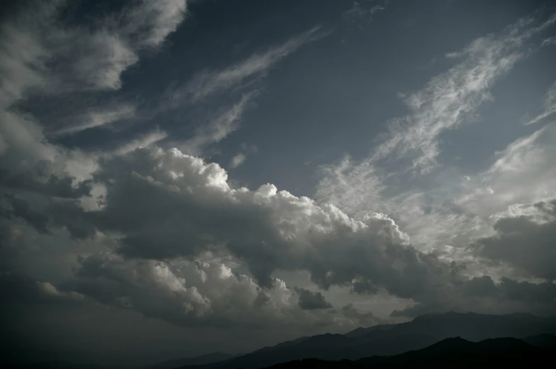 dark clouds hang over mountains under a sky that has lots of scattered white fluffy clouds