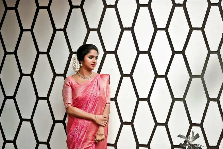 an indian woman wearing a pink dress and sari standing in front of a wall