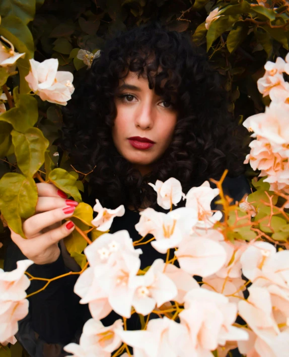 a woman with large black hair standing behind some flowers