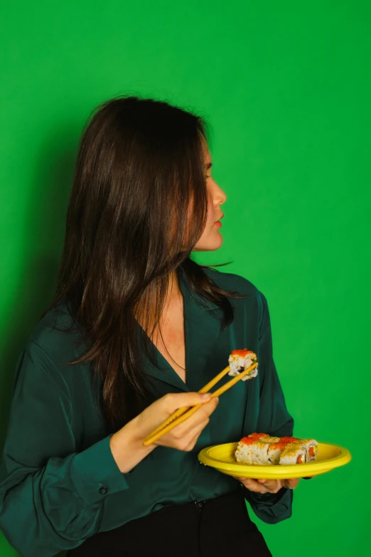 woman in a green shirt holding a plate and chopstick